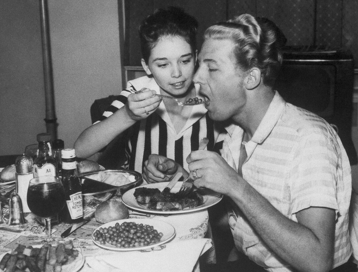 A young woman feeds a man a spoonful of peas.