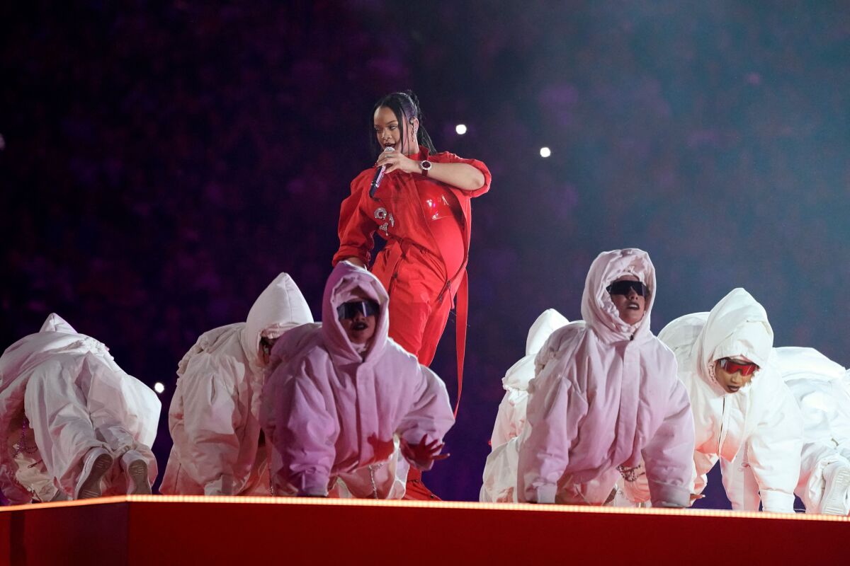 A woman in red performs onstage with backup dancers dressed in white