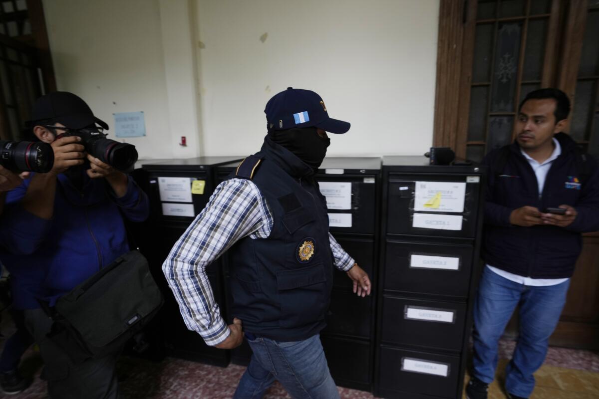 A masked member of Guatemala's attorney general's office walks through a room of boxes while others look on.