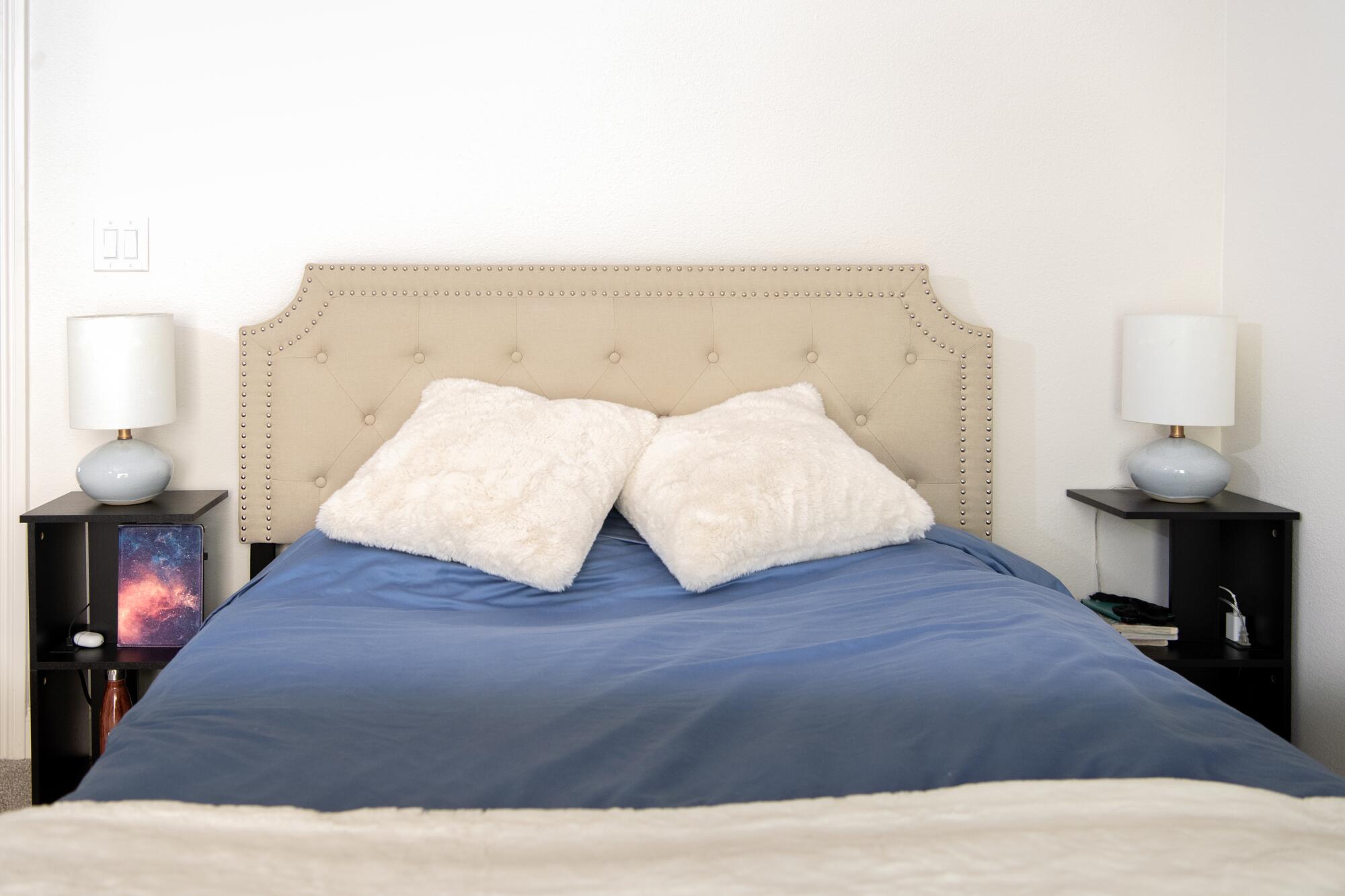 A bed with gray headboard, blue covers and white pillows in a bedroom.