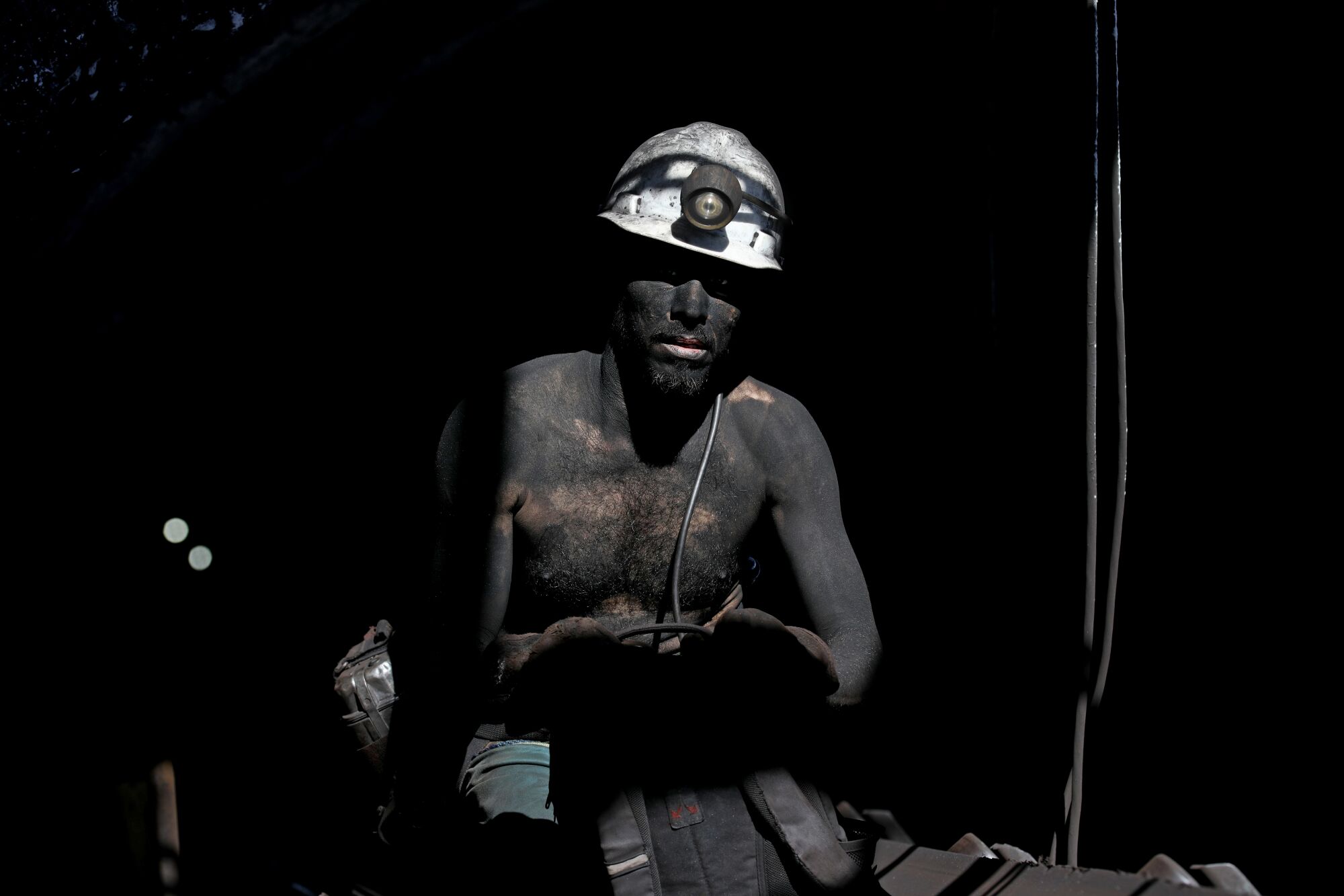 A man wears a mining helmet and is covered in soot.