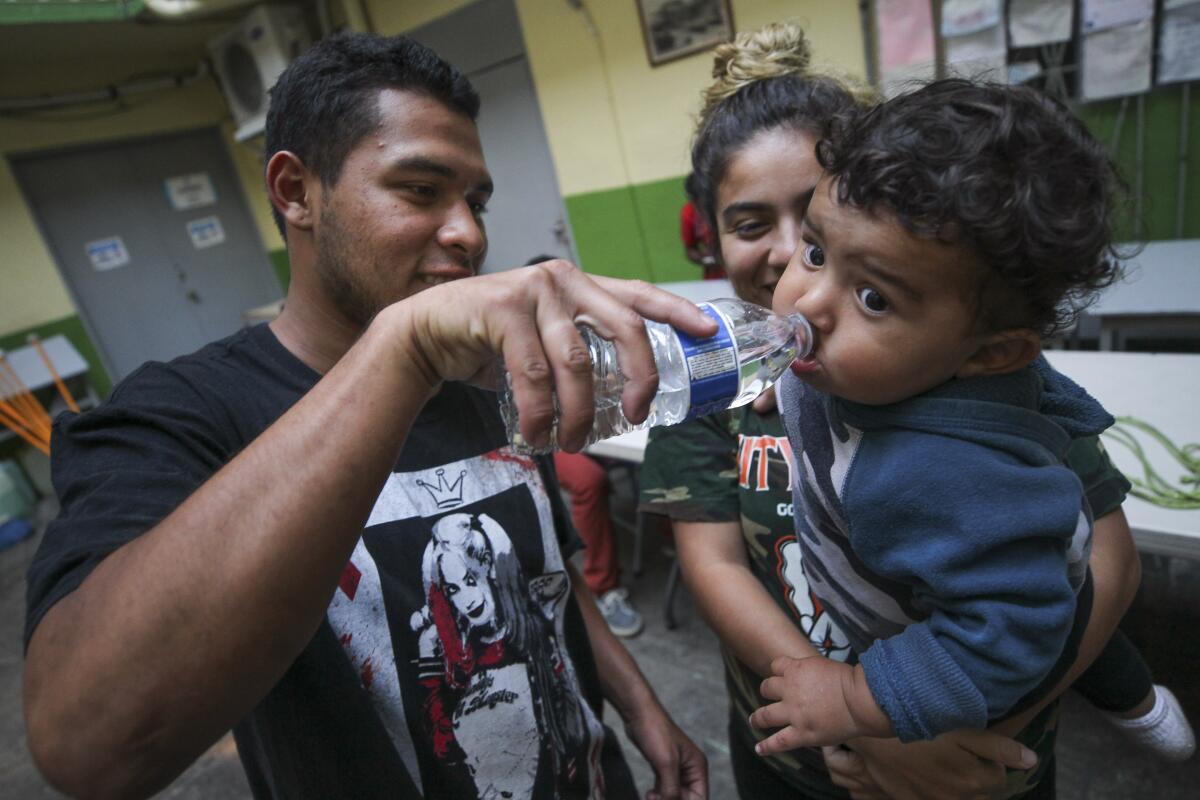 Helen Pérez sostiene a su hijo Miguel, de un año de edad, mientras su esposo Hans Vargas le da agua en Casa del Migrante, un refugio para migrantes, solicitantes de asilo y deportados, el viernes 16 de agosto de 2019 en Tijuana, México.