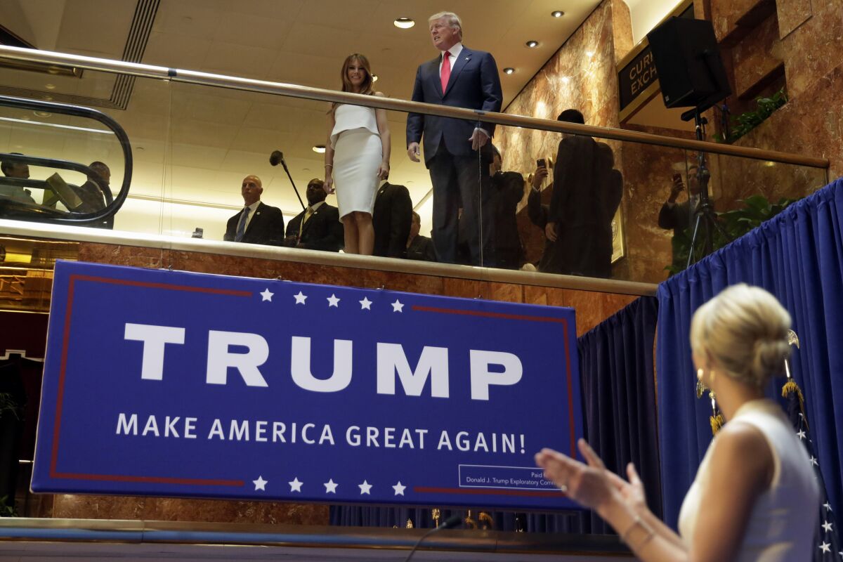 Donald Trump stands next to Melania Trump at the top of an escalator in Trump Tower. His daughter Ivanka Trump applauds.