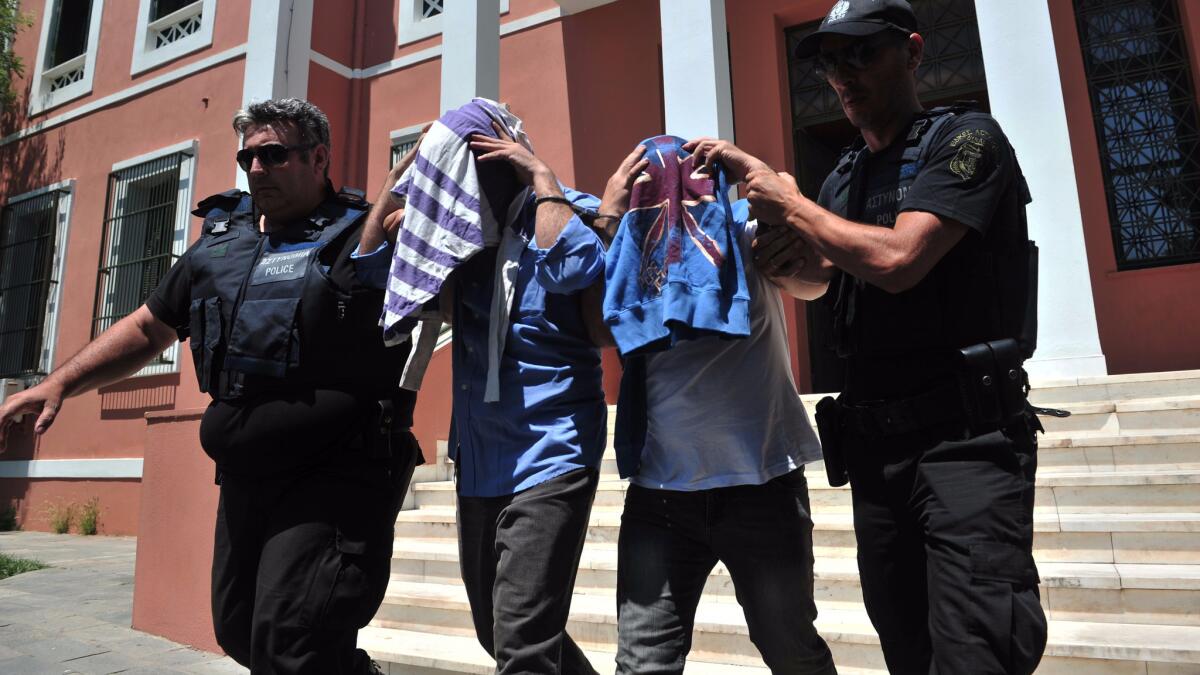 Greek police officers flank two Turkish military officers who appeared before a prosecutor in Alexandroupoli. They were among eight members of the Turkish military who flew to Greece in a helicopter and requested asylum.