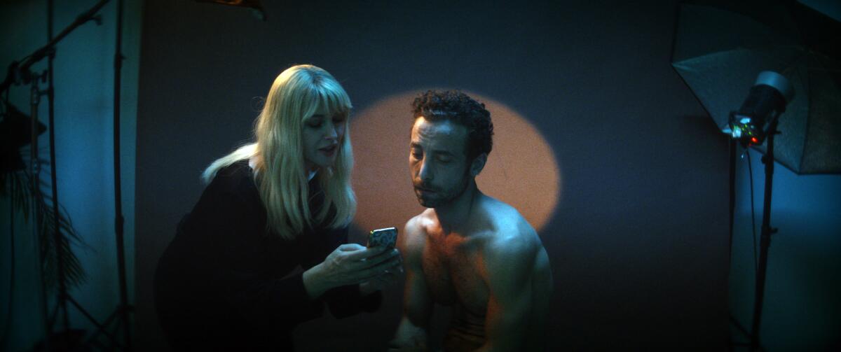 Two actors look at a phone in the movie "The Man Who Sold His Skin."