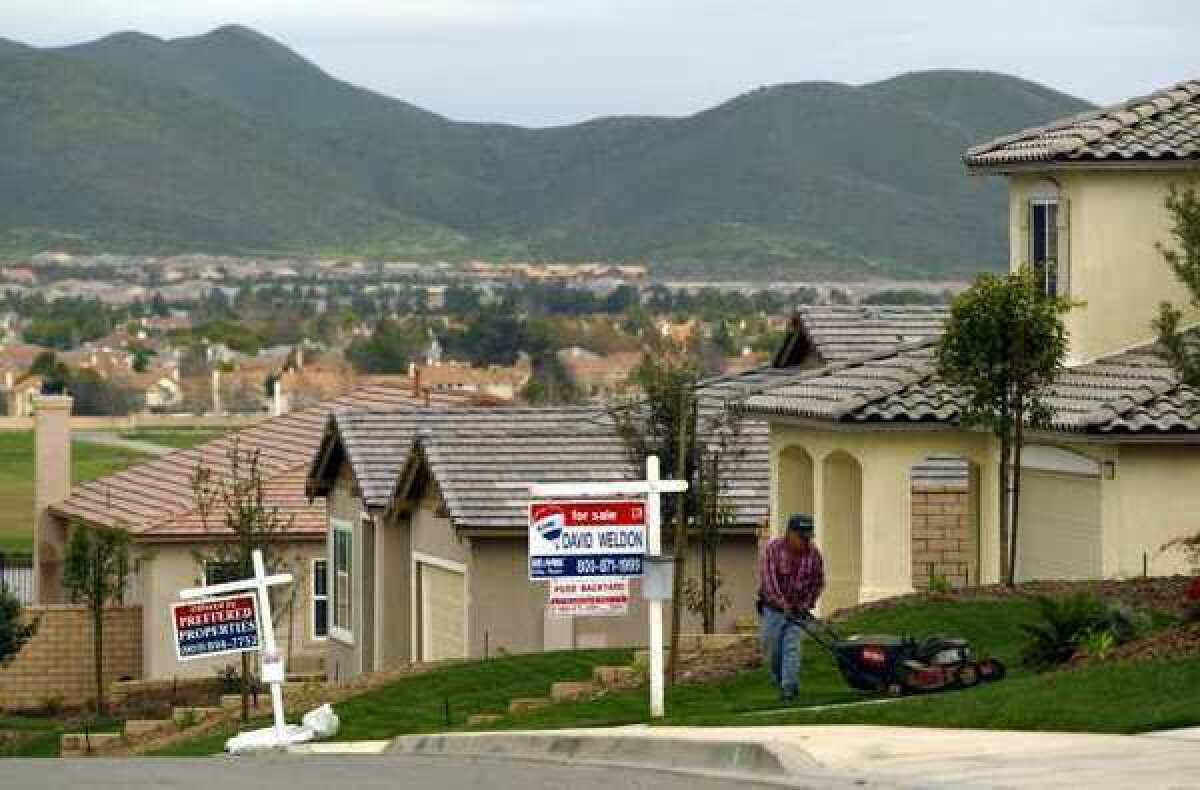 A man mows the lawn in front of homes with for sale signs out front