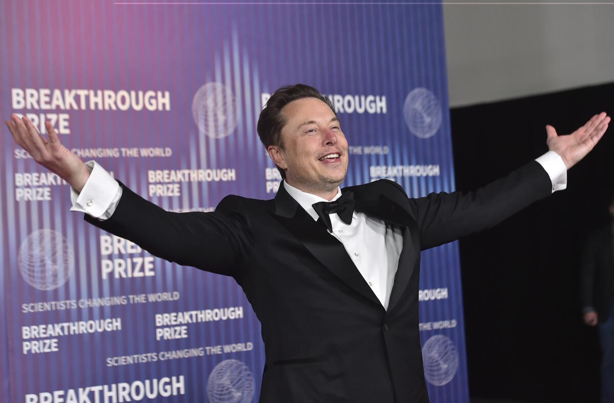 Elon Musk smiles with his arms spread wide.
