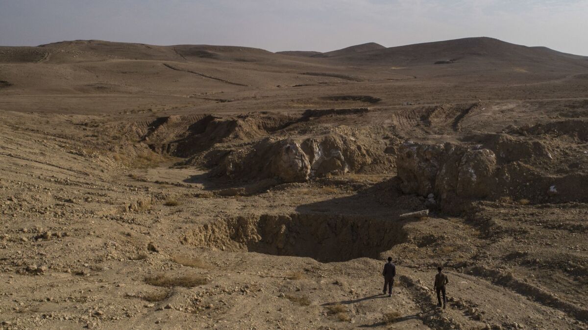 In this November 2017 photo, two Iraqi men walk near a sinkhole known as Khasfa that is believed to contain the remains of people executed by Islamic State militants south of Mosul, Iraq.
