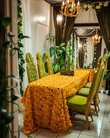 A meeting room in a store with a bright orange tablecloth and six green upholstered chairs, surrounded by plants.