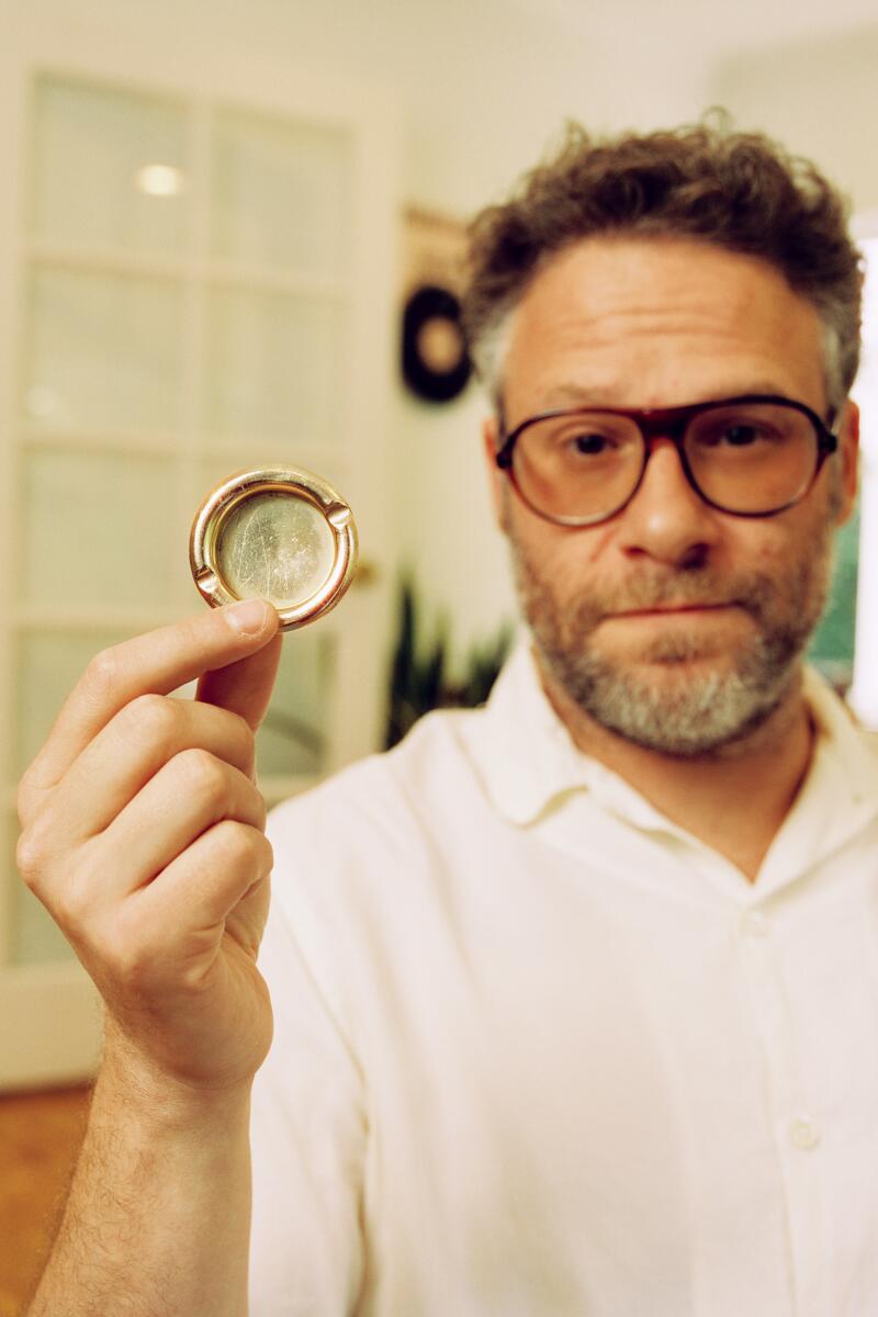 Seth Rogen holds up a small circular ashtray.
