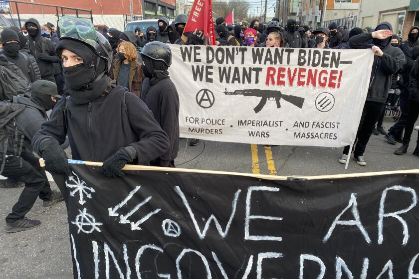 Anarchists march in Portland Wednesday, carrying a banner opposing President Joe Biden.