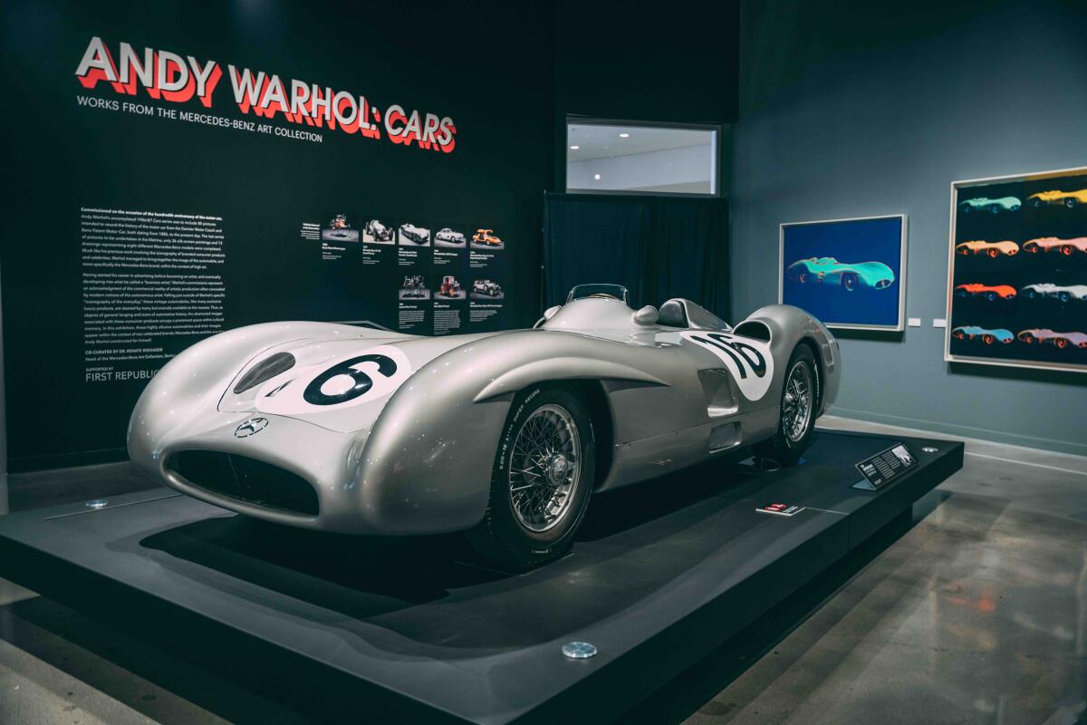 A Mercedes-Benz car and paintings of cars pictured in a gallery.