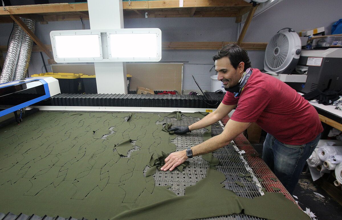 LiquidSky Sports owner Julio Ruiz sweeps up mask patterns that have been laser cut at LiquidSky Sports on Tuesday. The Burbank business shifted its manufacturing from sports apparel, particularly skydiving suits, to making uncertified N95 masks using a custom mask pattern, a modified A/C filter, and copper wiring for fit due to a shortage on all mask supplies.