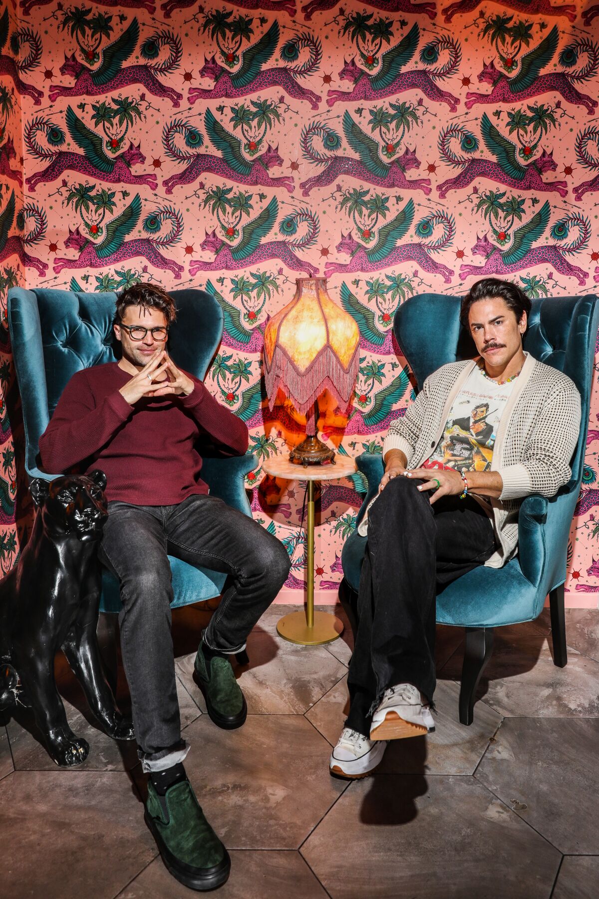 "Vanderpump Rules" stars Tom Sandoval and Tom Schwartz sit in arm chairs in front of a pink and green patterned wall.