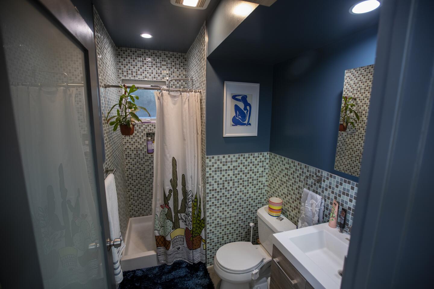 A small bath with shower, rectangular vanity and mirror . Small tile reaches halfway up the walls.