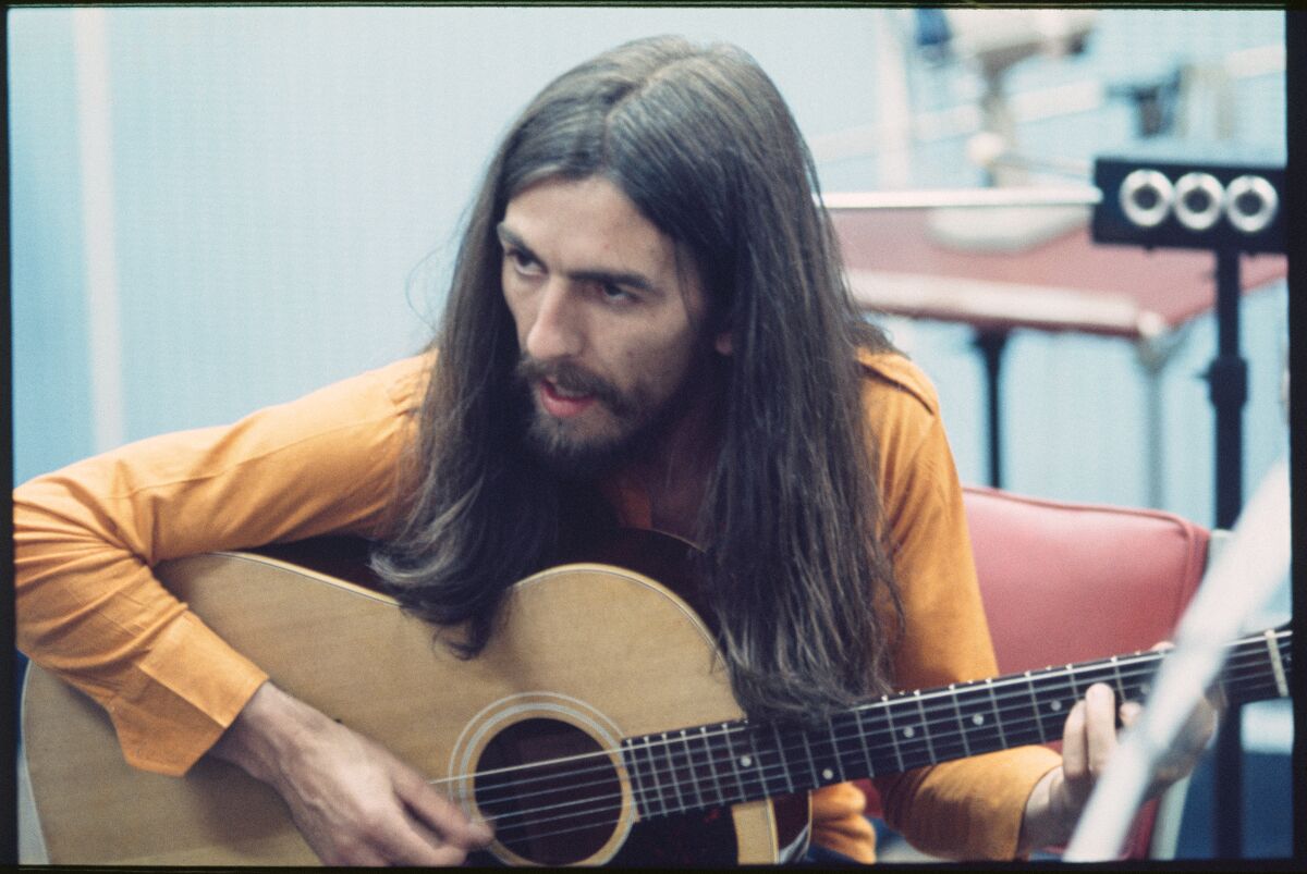 George Harrison plays a guitar while seated.