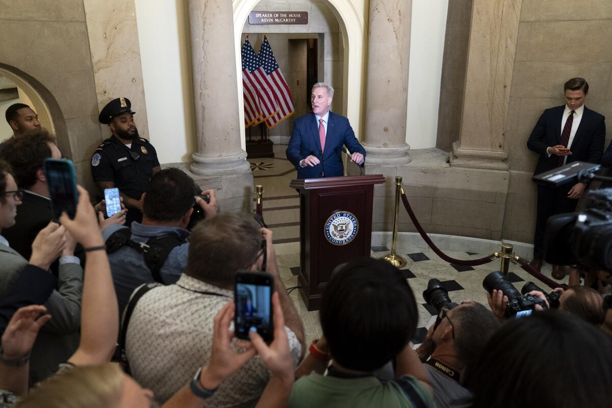 The back of a crowd with phones and cameras looking at a person at a podium.