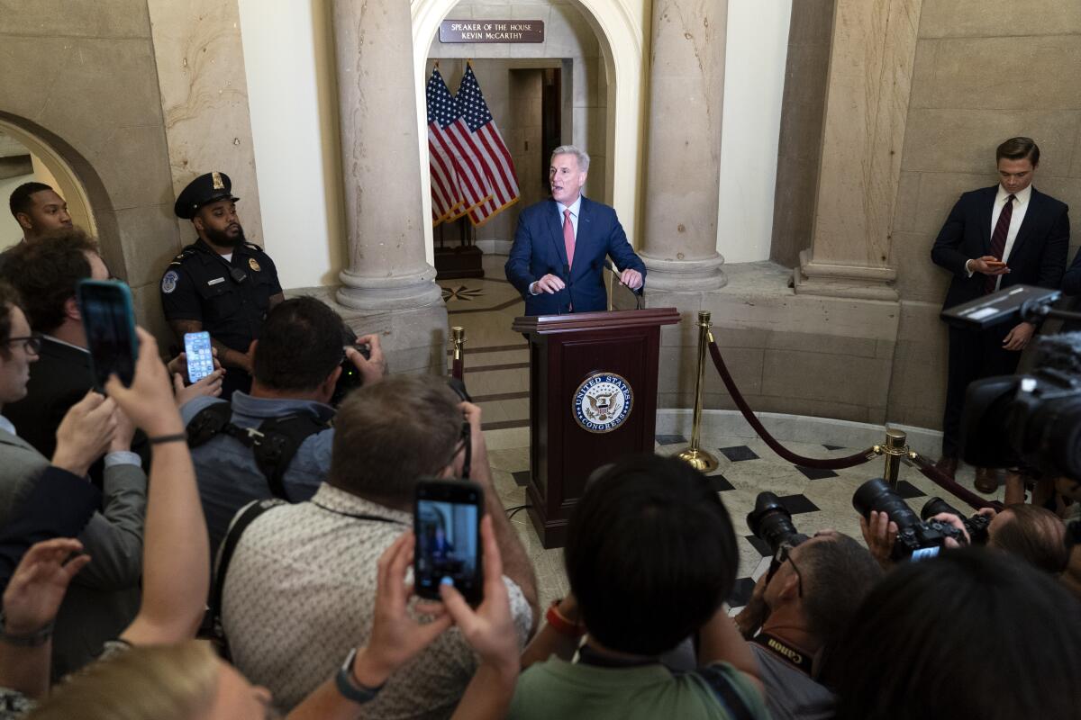 The back of a crowd  with phones and cameras looking at a person at a podium.