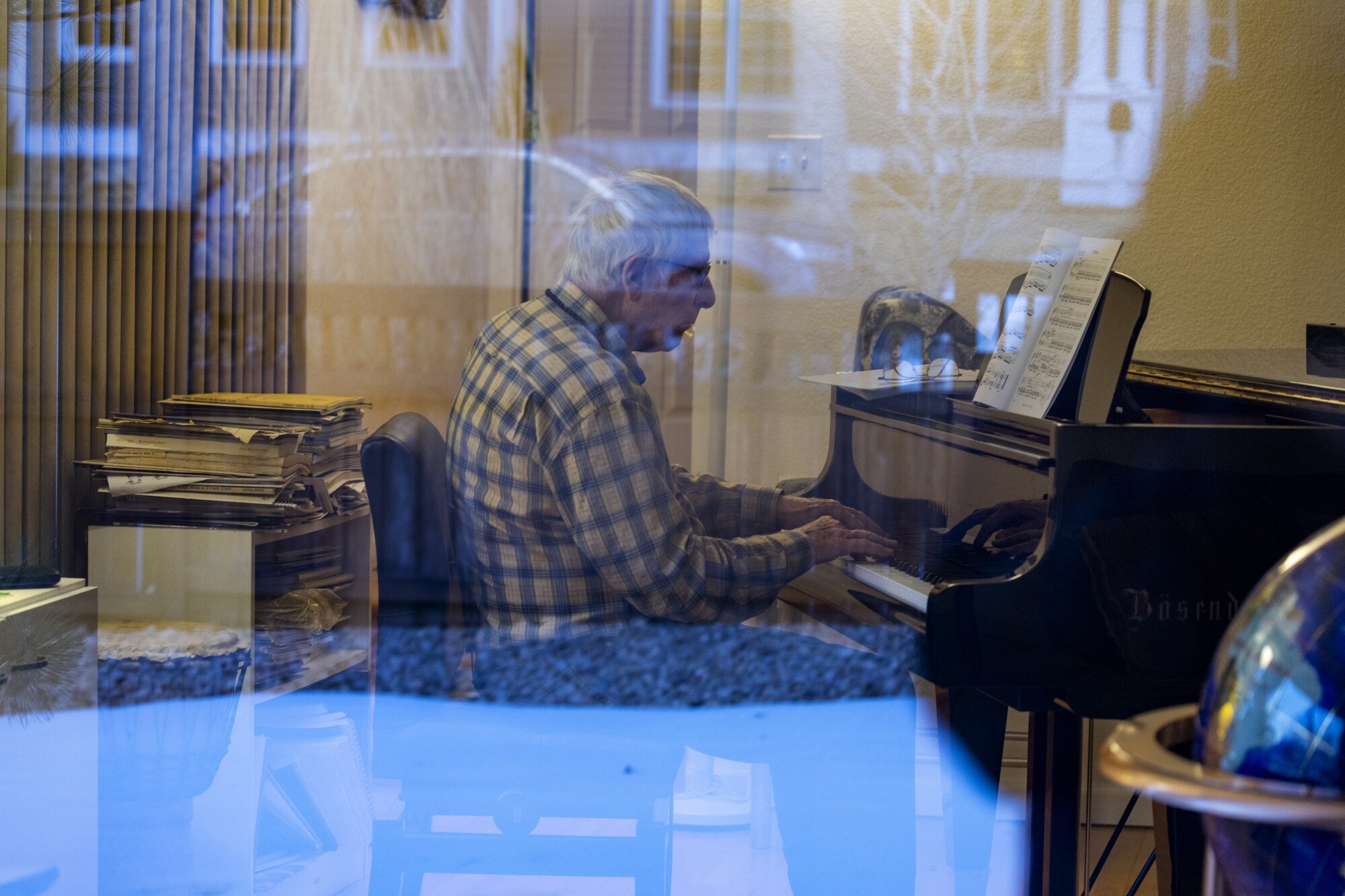 Reflections are cast on a window as Dr. Warren Hern plays the piano.