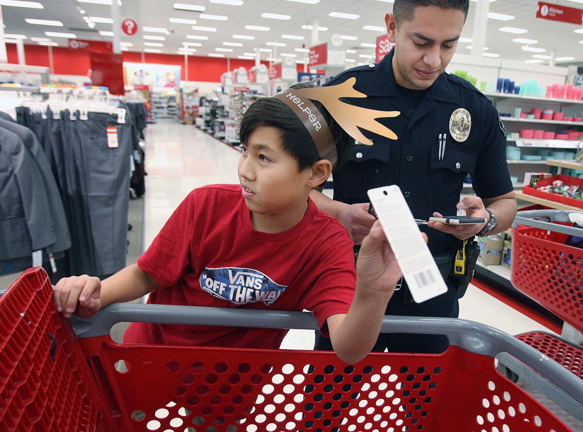 Sean Kang, 10, shows a gift he found to a friend while his shopping partner, Burbank Police Officer Jorge Jaime, calculates how much Sean has left to spend at Target for the "Shop with a Cop" event on Thursday, Dec. 8, 2016.