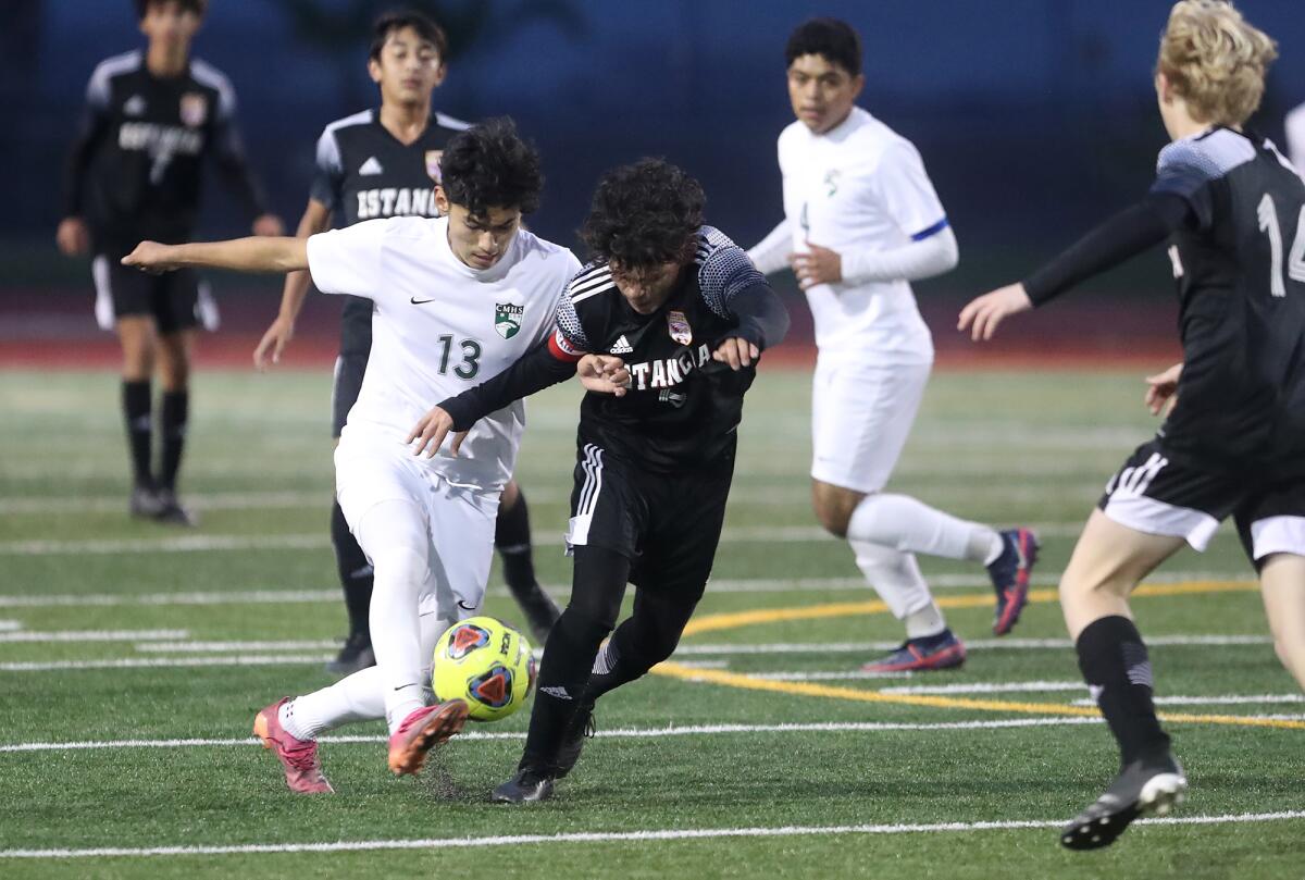 Costa Mesa's Gabriel Garcia (13) and Estancia's Cruz Valdovinos do battle in the midfield for ball control on Friday.