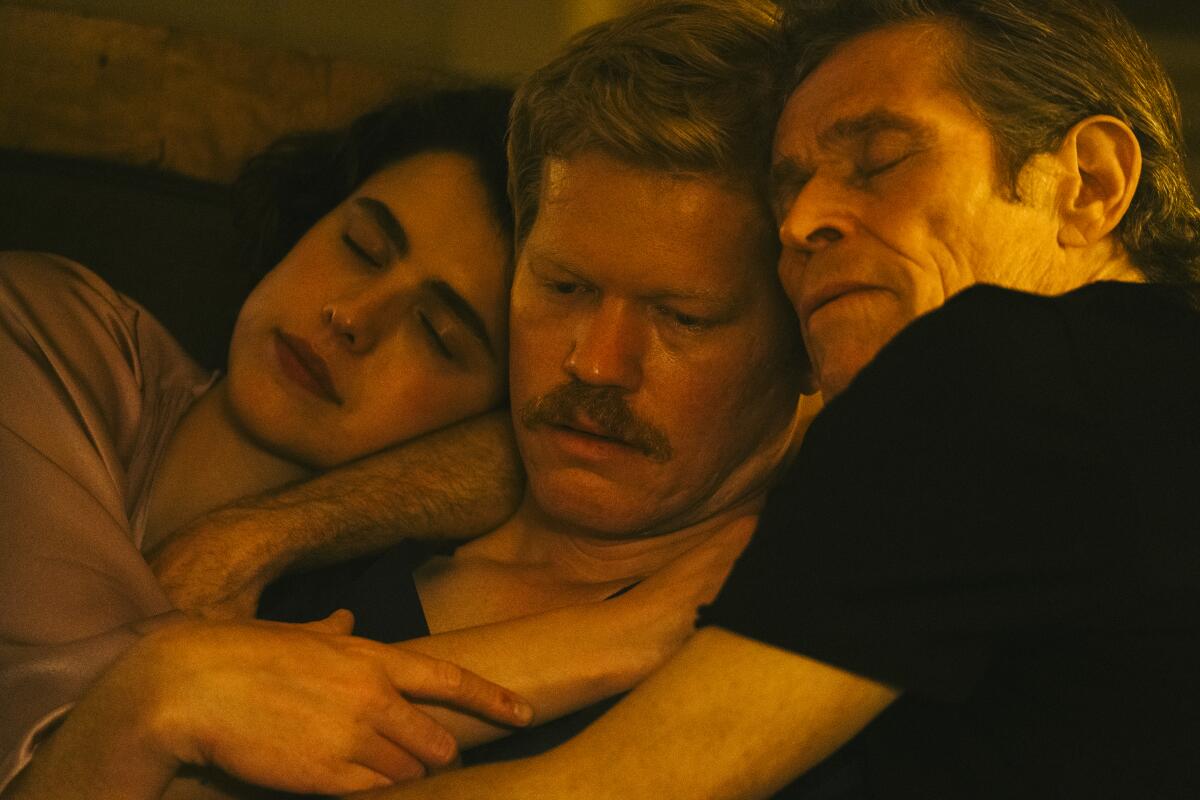 Three adults hug in bed.