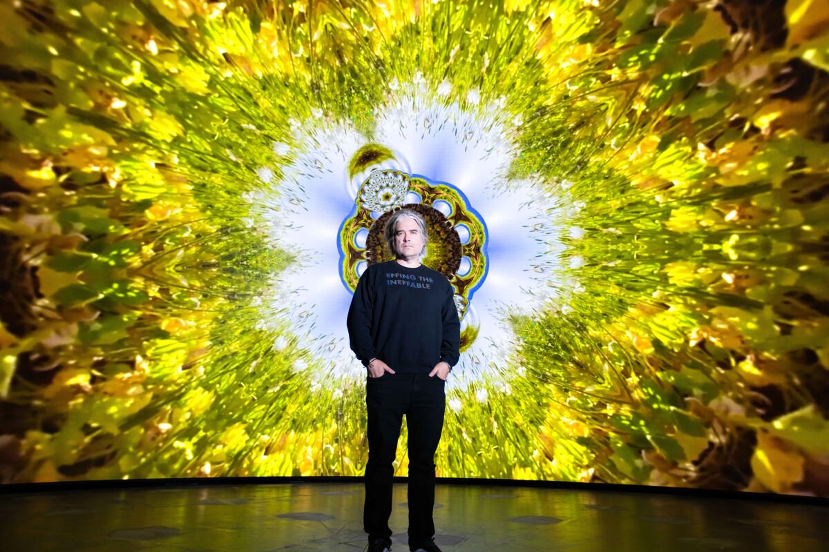 Artist Chris Holmes wears a navy sweatshirt and stands in front of his vibrant art piece.