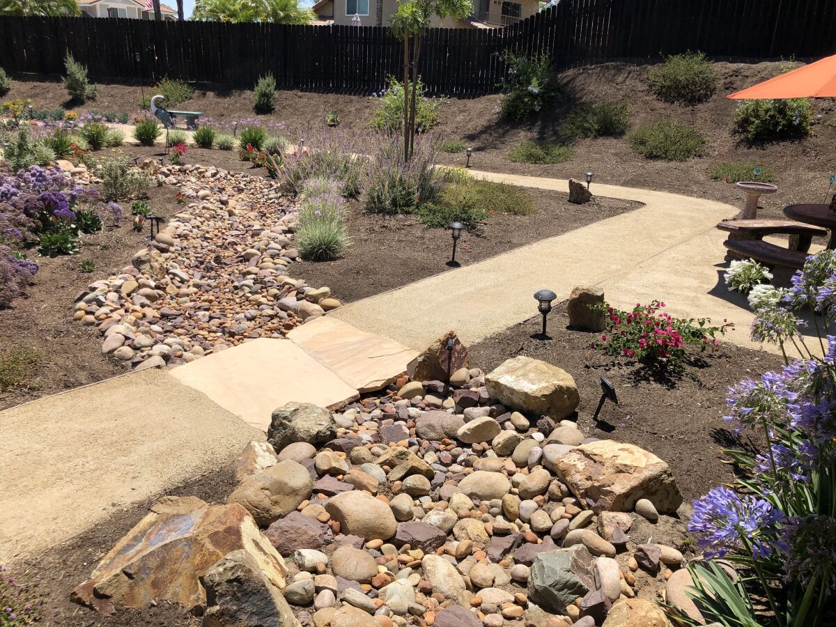 A garden path crosses the stone-lined dry creek bed, accented by solar lights that illuminate it at night.