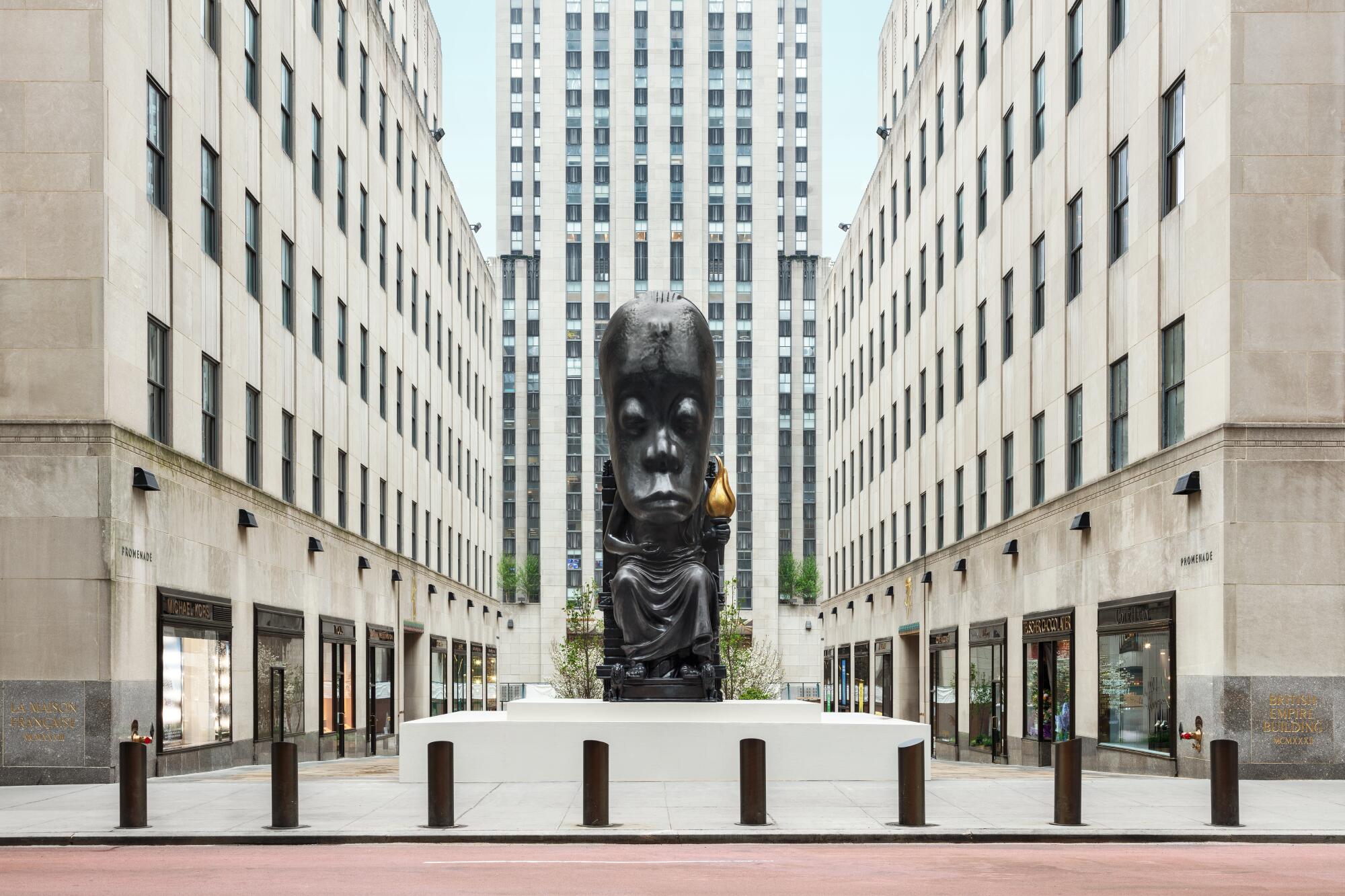 A bronze sculpture shows a seated, European-style figure bearing a torch with an oversized African mask for a head.