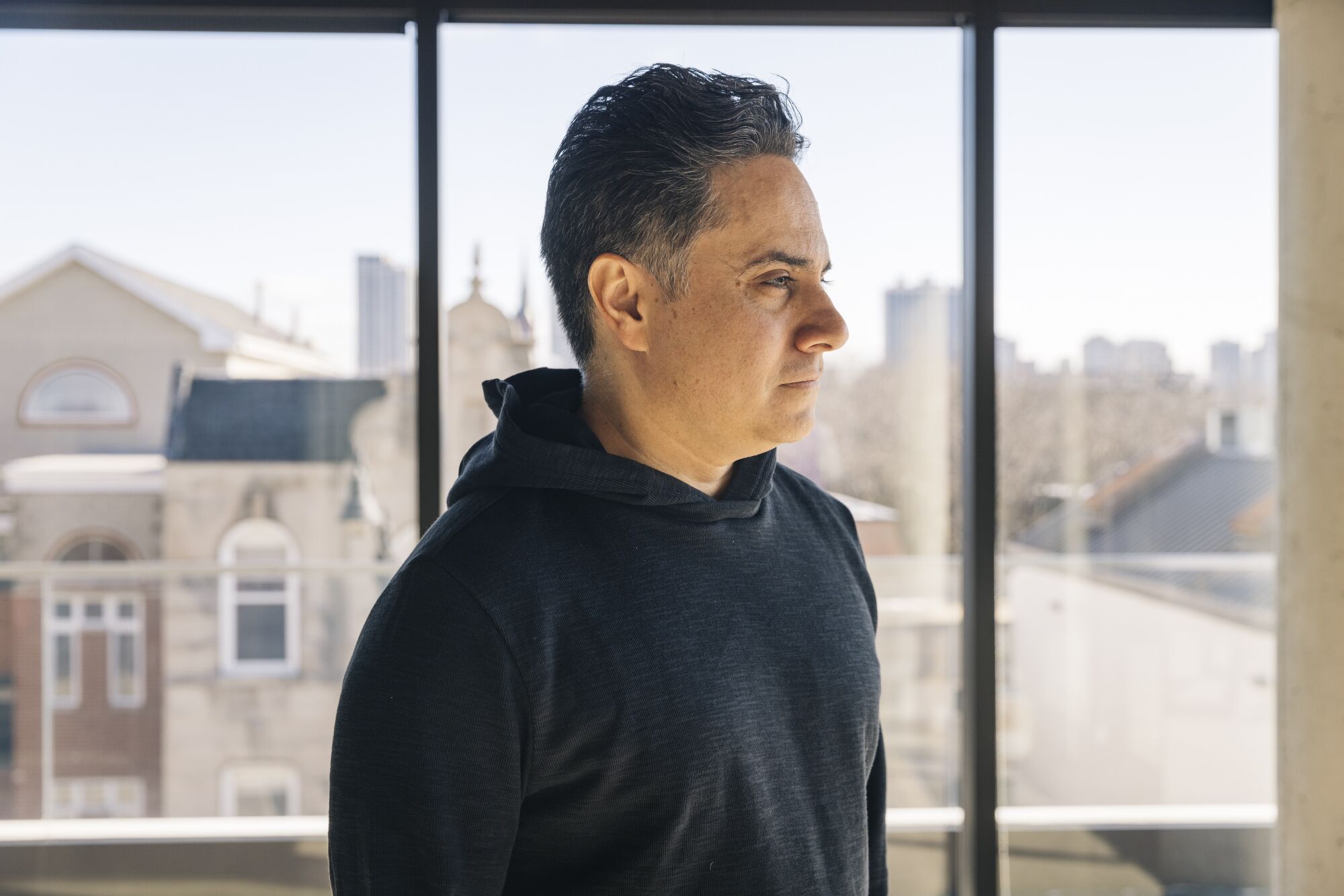 A portrait of playwright Rajiv Joseph, standing in profile against a bank of windows.