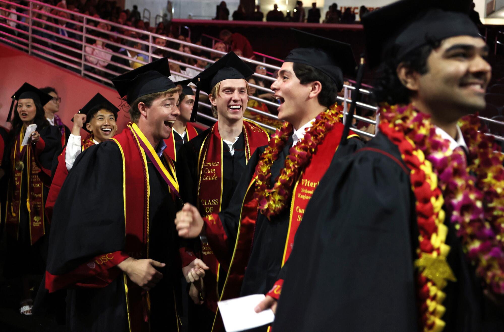 USC graduates smile together in black gowns, mortarboards and sashes with the university's cardinal and gold colors