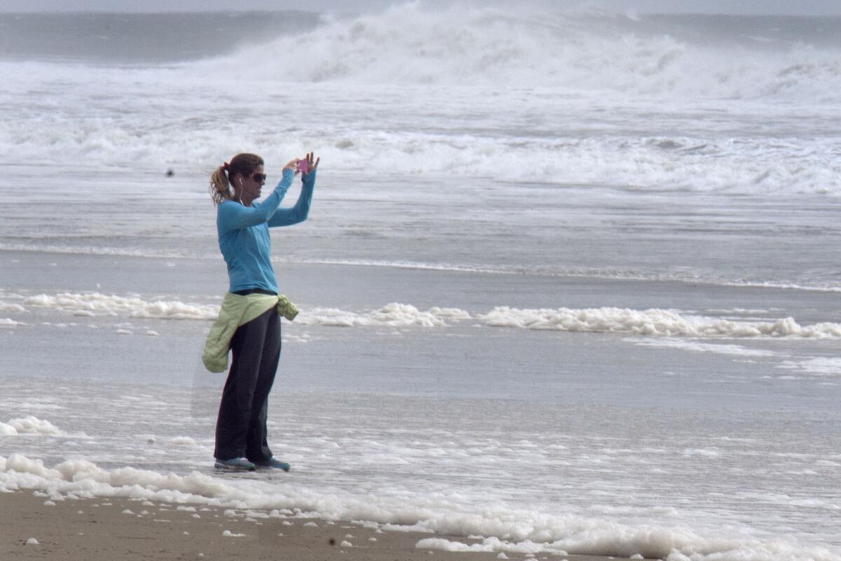 Socorro Hubbard takes pictures of the waves after her walk at Huntington Beach on Saturday. The storm-powered waves reached 8 to 12 feet.