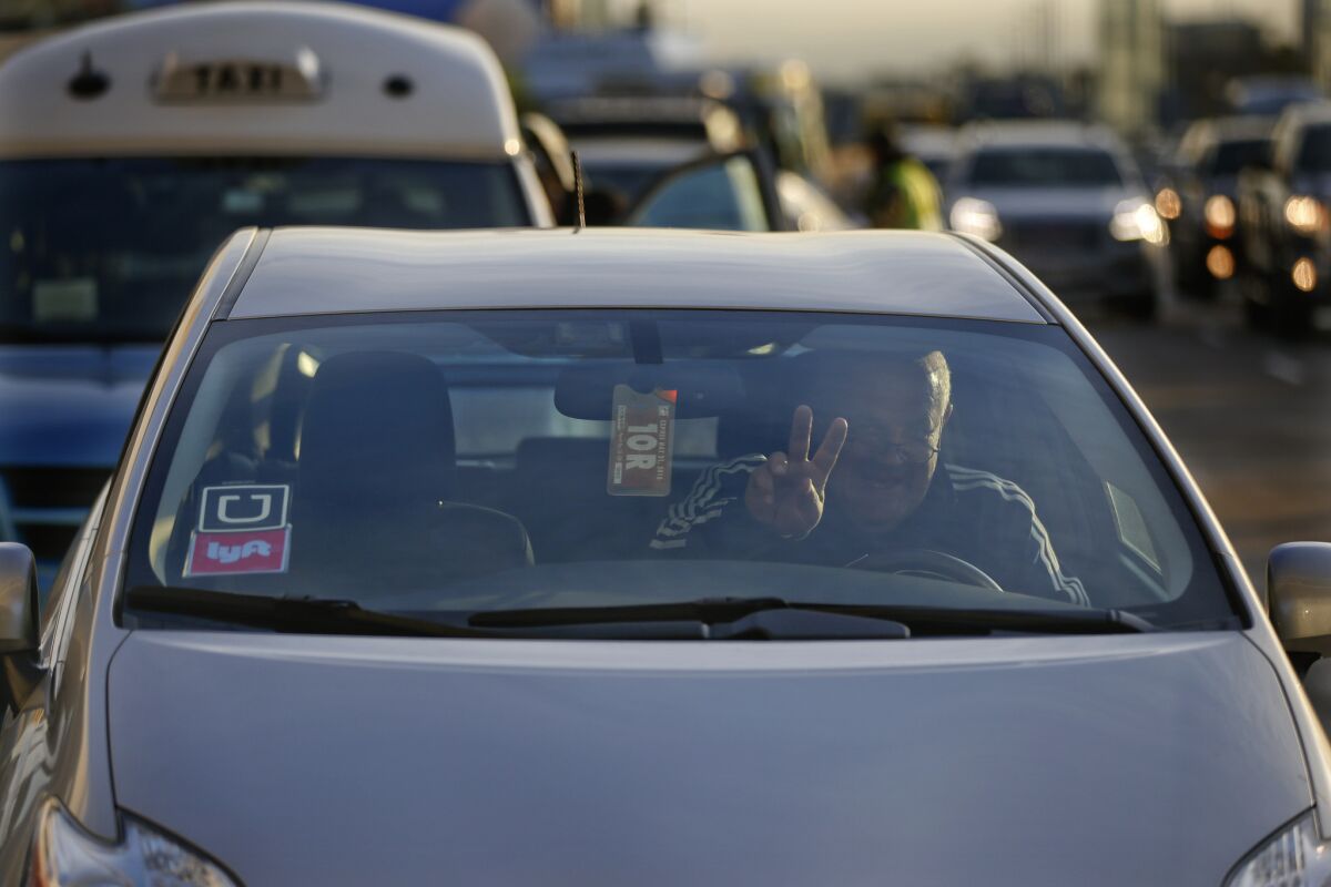 A driver for Uber and Lyft flashes a peace sign as he navigates traffic at Los Angeles International Airport in December.