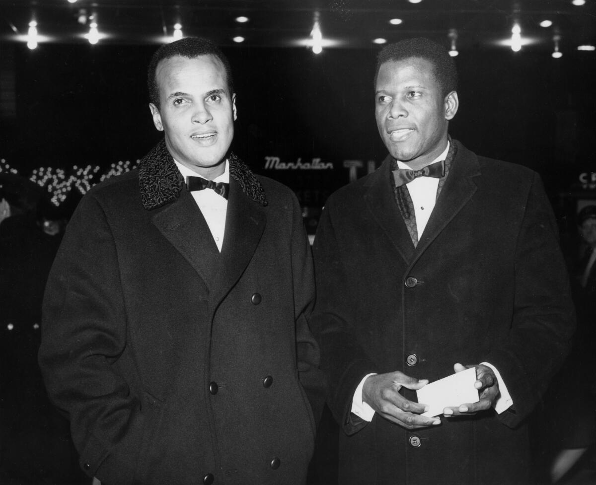 Actor and singer Harry Belafonte and Sidney Poitier stand side by side while wearing tuxes.