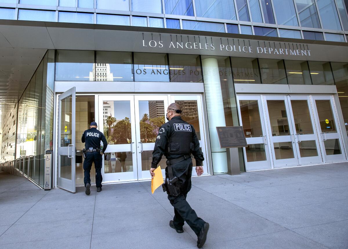 Two men in black police uniforms walk toward a row of glass doors with a "Los Angeles Police Department" sign above.