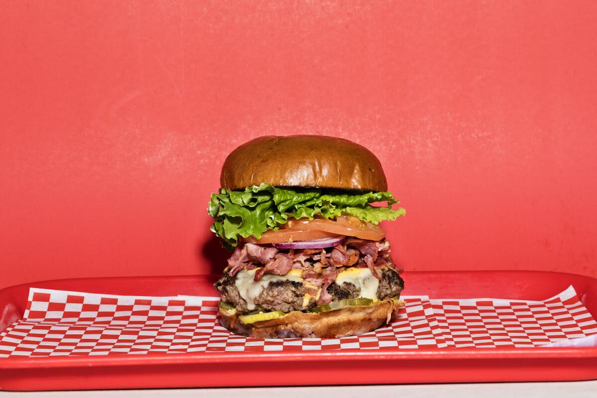 A fully stacked hamburger on red-and-white checkerboard paper on a red tray