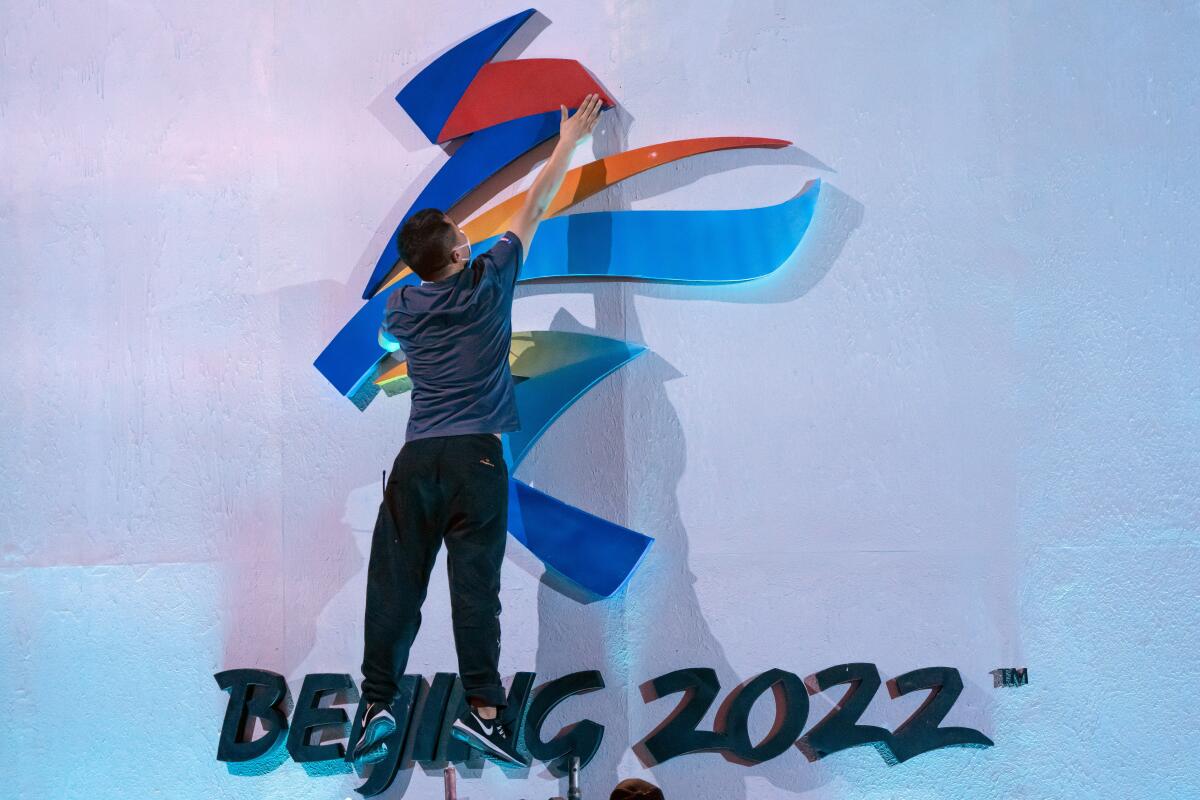 Un miembro del personal salta para reacomodar un logo de los Juegos Olímpicos de Invierno Beijing 2022 
