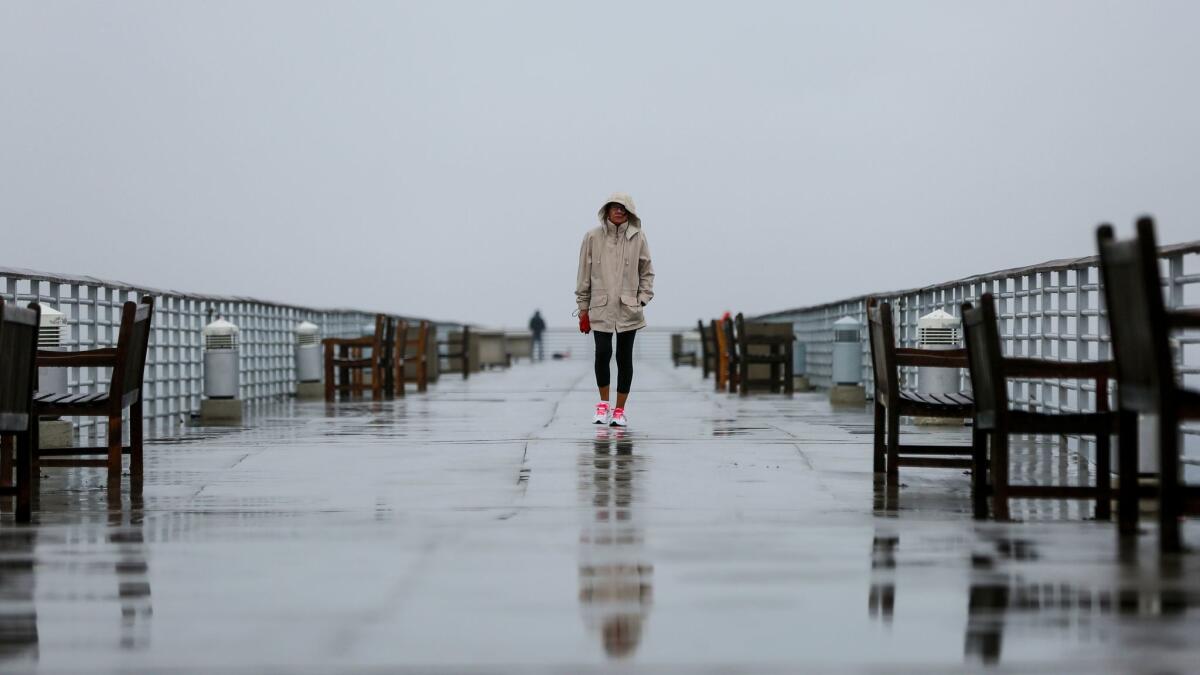 A woman walks along the Hermosa Beach Pier last week during a lingering rainstorm.