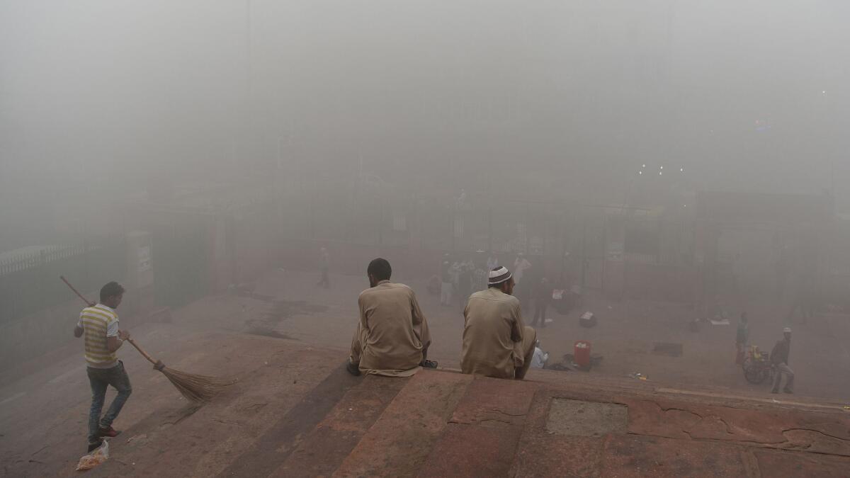 Indian visitors sit on the steps outside Jama Masjid amid heavy smog in New Delhi.