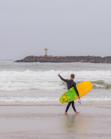 A surfer walks along the shoreline of Avalanche at Ocean Beach in San Diego, California. Photographed in June 2024.