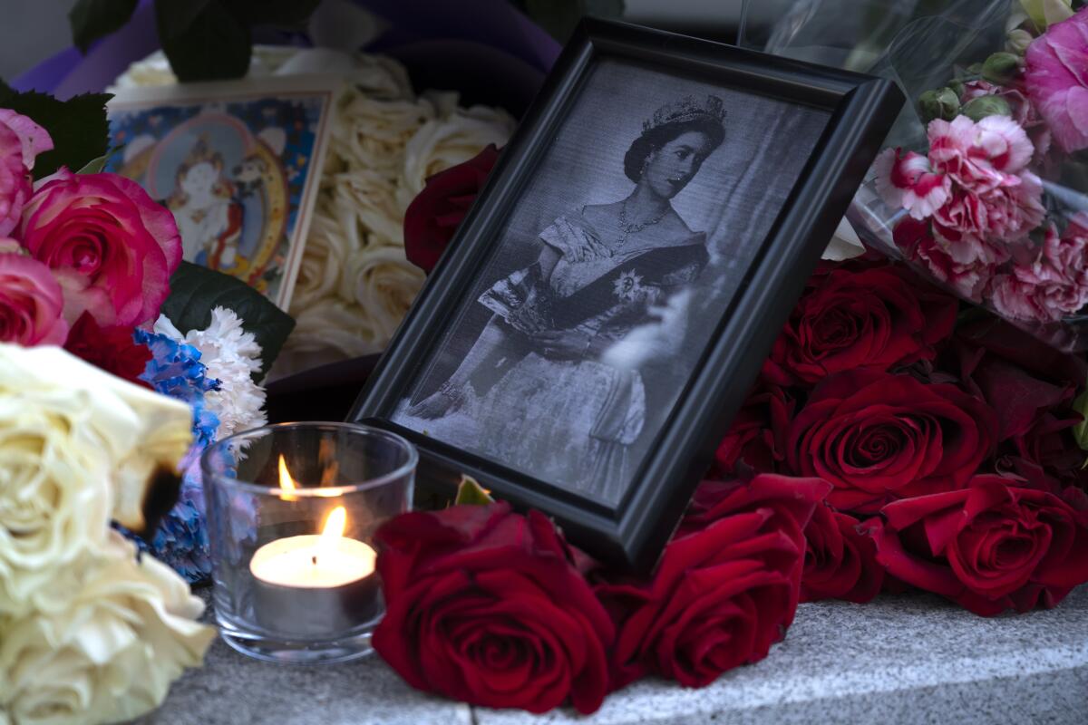 A portrait of Queen Elizabeth II, a candle and flowers in remembrance of her Majesty are seen at the Embassy of the United Kingdom in Moscow, Russia, Friday, Sept. 9, 2022. Queen Elizabeth II, Britain's longest-reigning monarch and a rock of stability across much of a turbulent century, died Thursday after 70 years on the throne. She was 96. (AP Photo/Dmitry Serebryakov)