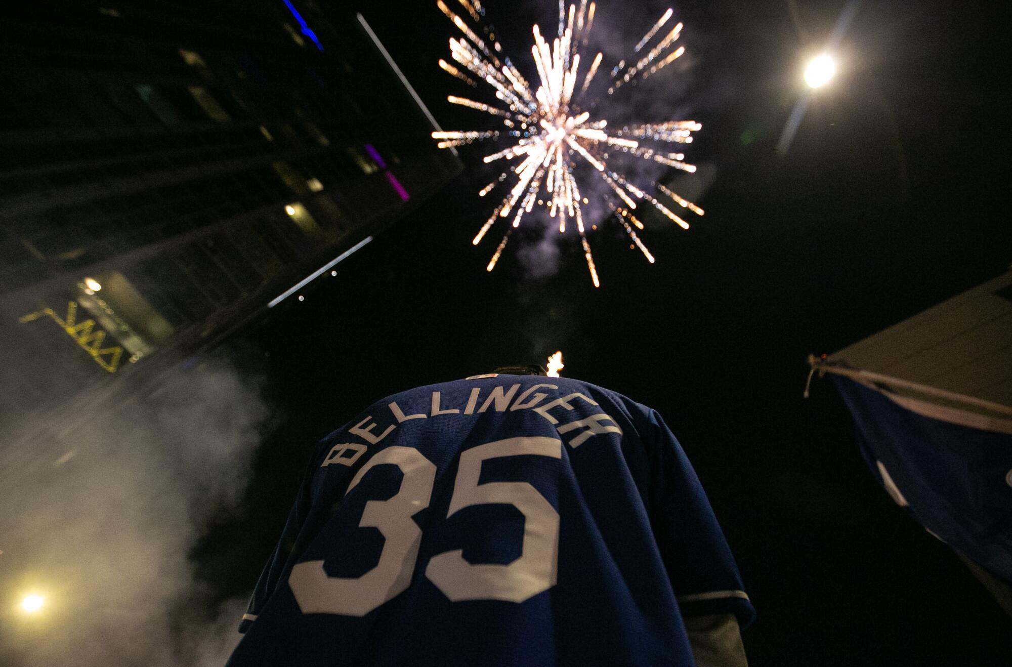 Fireworks explode in the sky above a fan in a Bellinger jersey.