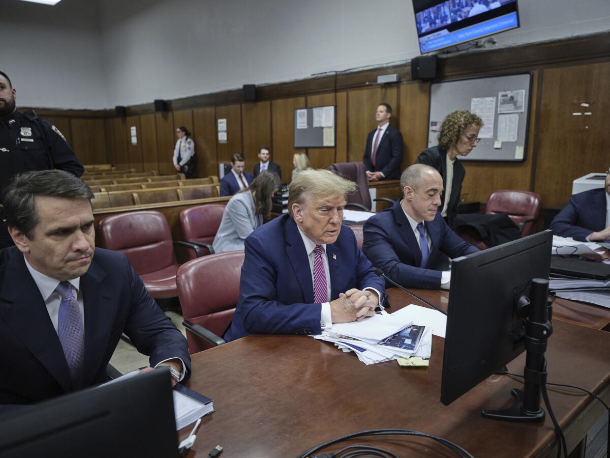 Former President Trump sits at a table between lawyers in Manhattan criminal court. 