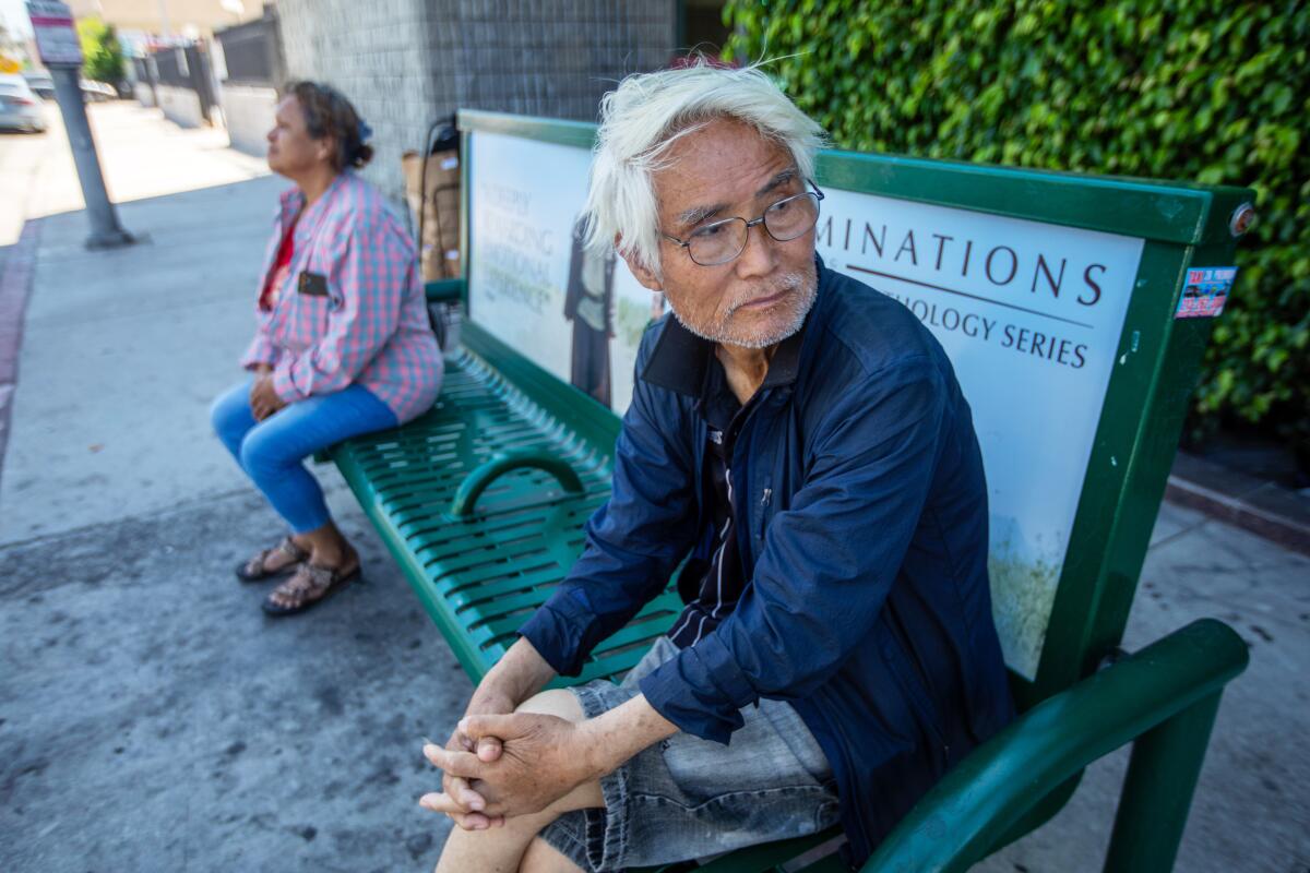 A man sits on a bench waiting for the bus in Koreatown.