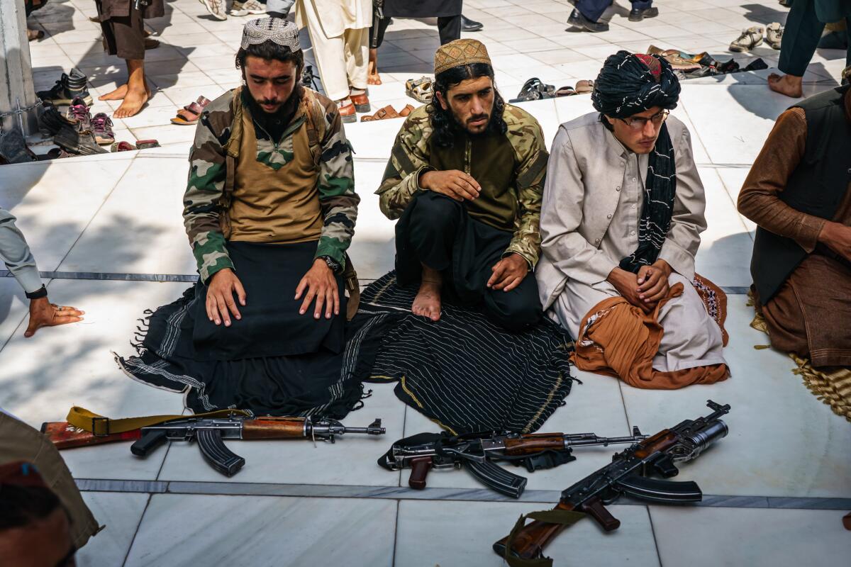 Taliban fighters kneeling alongside their weapons for Friday prayers