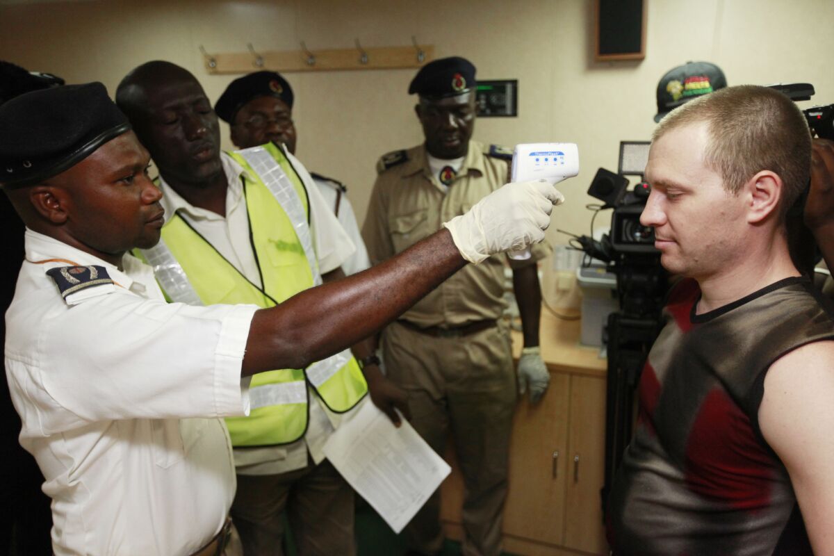 A Nigerian port health official, left, uses a thermometer to screen an unidentified Ukrainian crew member, right, for Ebola on the deck of a cargo ship at the Apapa port in Lagos, Nigeria.