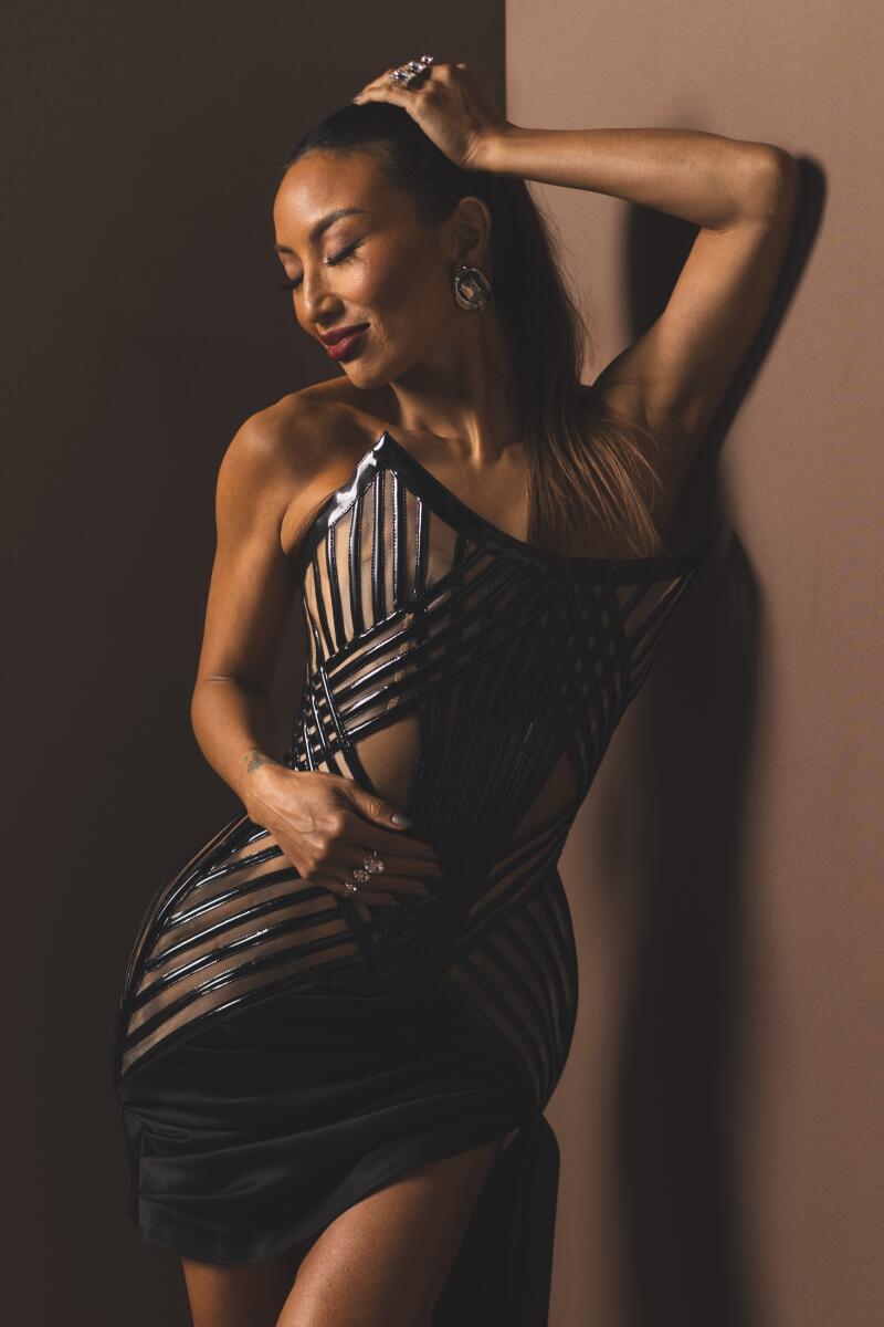 Jeannie Mai Jenkins leans against the wall with one arm and looks down, her eyes semi-closed.
