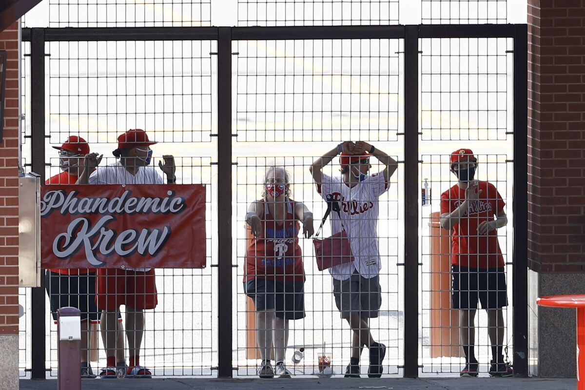 FILE - In this Aug. 5, 2020, file photo, Philadelphia Phillies fans watch from an outfield gate during the first inning of the first baseball game in doubleheader against the New York Yankees, in Philadelphia. The Phandemic Krew are the Phillies biggest fans.(AP Photo/Matt Slocum, File)