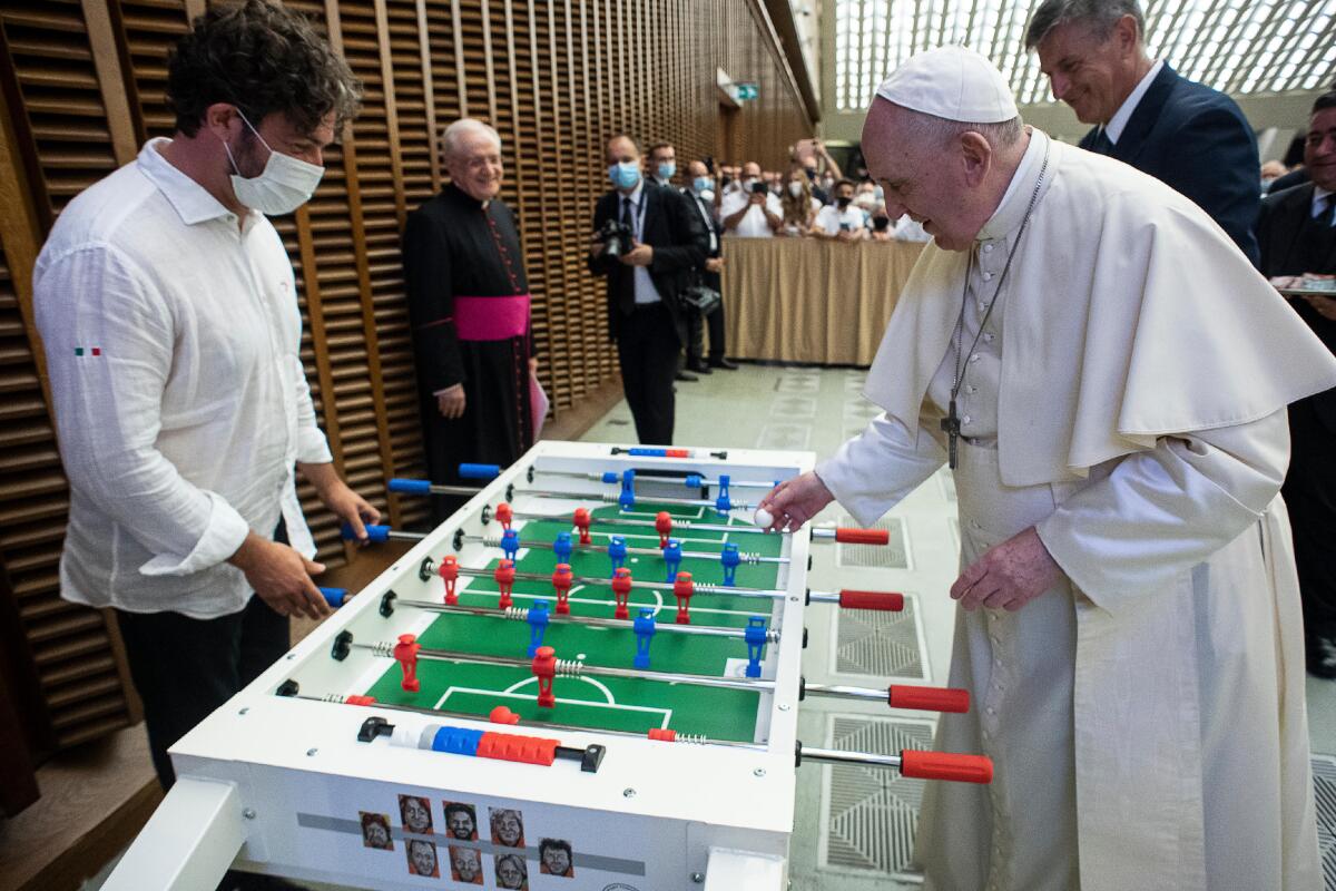 Pope Francis plays with Natale Tonini, president of Sport Toscana Calcio Balilla association, at the end of the weekly general audience, Wednesday, Aug.18. 2021. Francis played a round on the table that was presented to him by representatives of a the association, that created a special Foosball table designed to be inclusive, for people with physical disabilities, to encourage their participation in sport. (Vatican Media via AP)