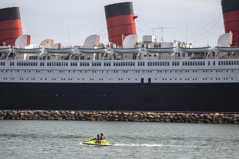 Long Beach, CA - May 25: Two people on a jetski are seen in the water, with the Queen Mary ship in the distance, docked in Long Beach, CA, photographed Tuesday, May 25, 2021. The ship has been a tourist destination and hotel for years and is now in danger of capsizing according to a recent inspection report. (Jay L. Clendenin / Los Angeles Times)